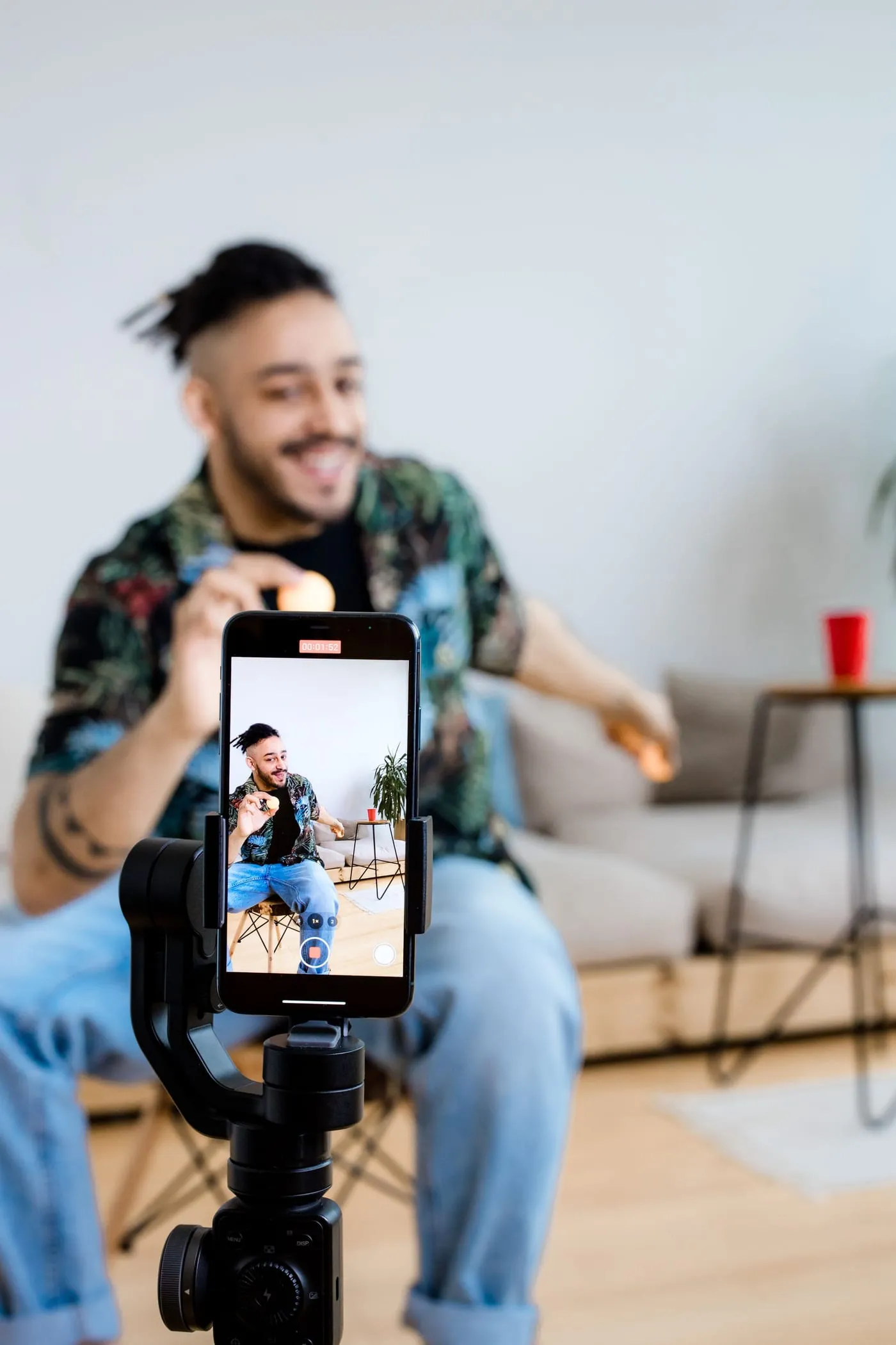 A creator records himself with a phone mounted on a stabilizer in a home studio.