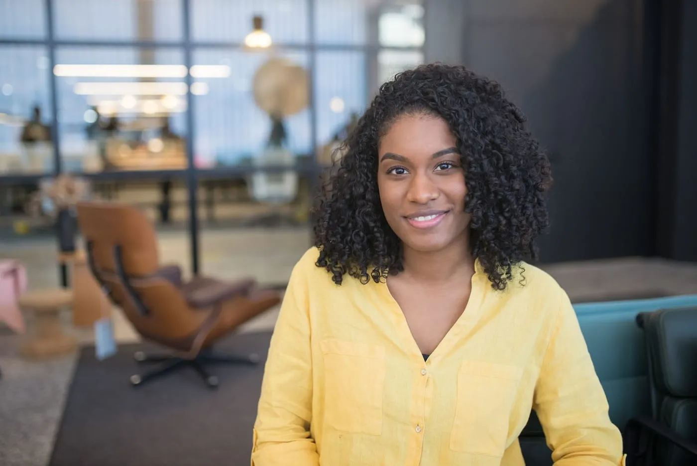 A woman in a yellow blouse smiles in a bright, modern office.